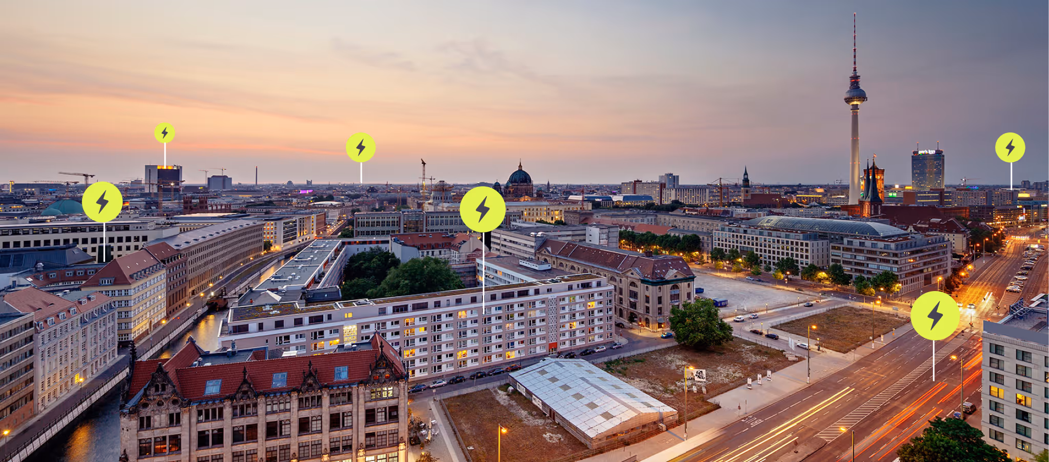 Cityscape at dusk with illuminated buildings, streets, and icons indicating electric charging points.