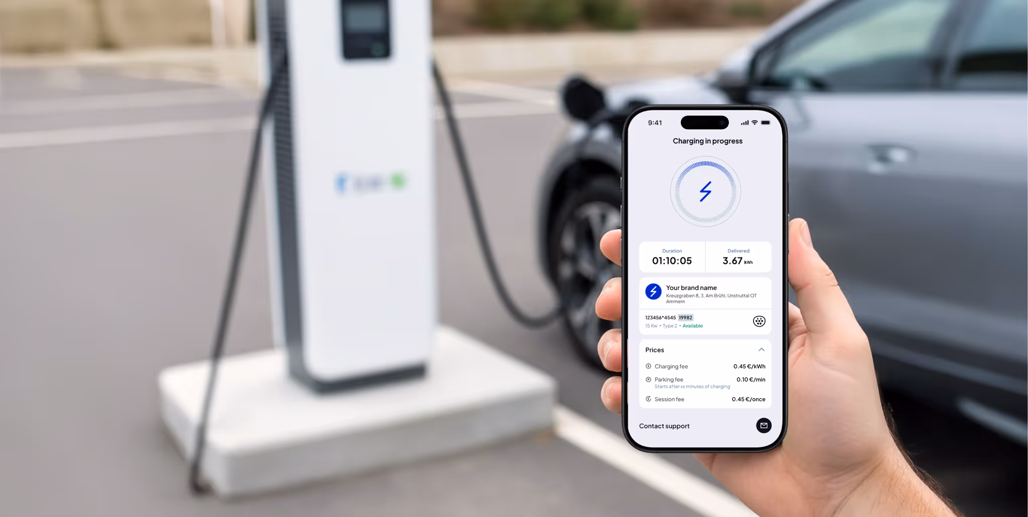 Hand holding smartphone displaying electric vehicle charging app with charging progress and pricing details, near a charging station and a parked car.